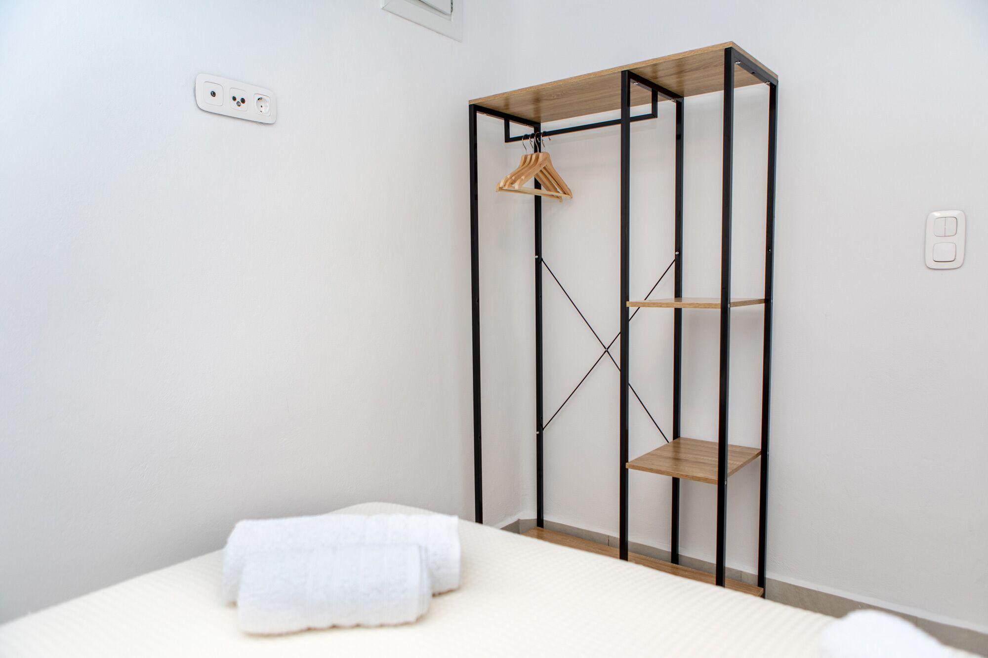 Een slaapkamer met een bed, een houten garderobe met planken en een kledingrek.