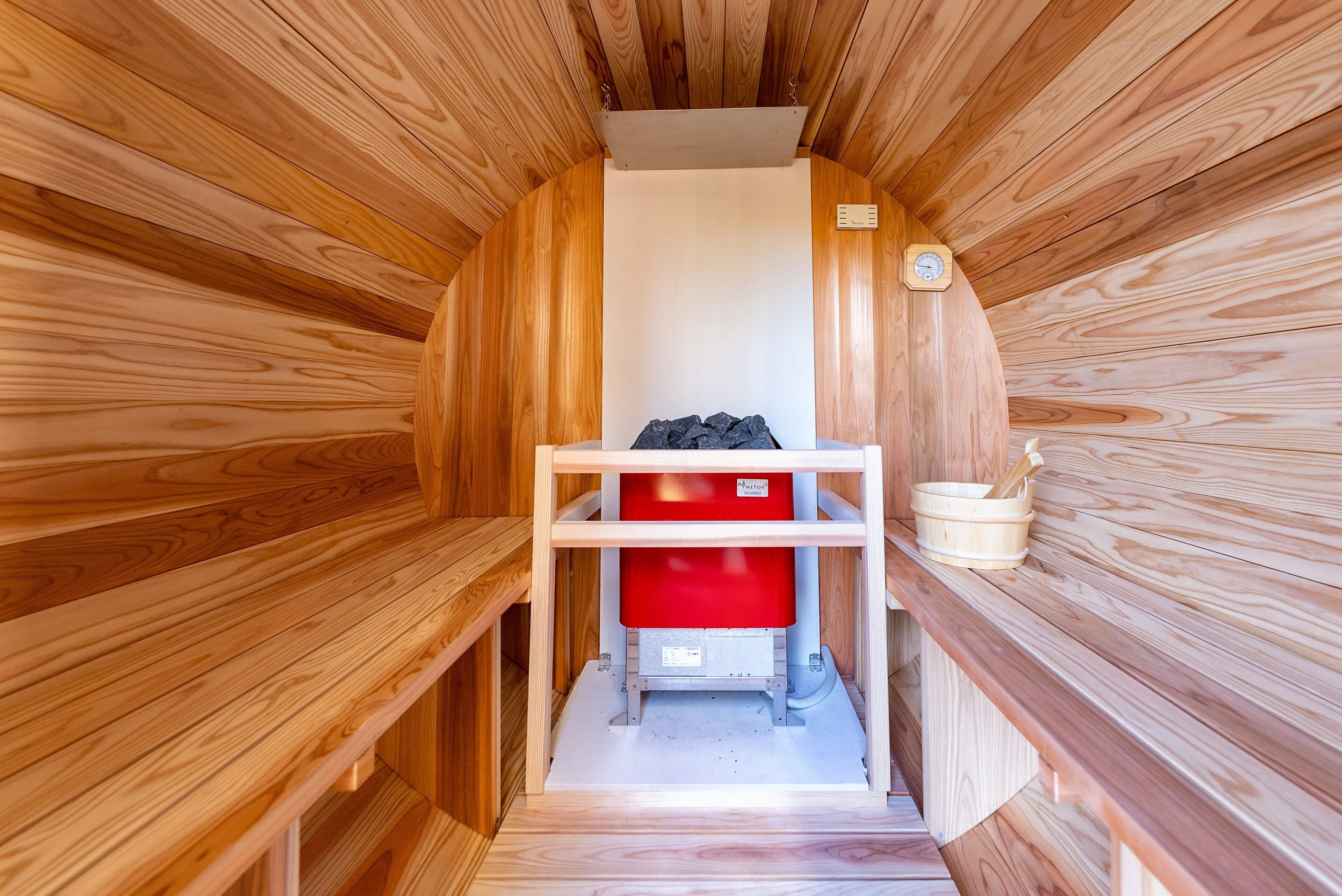 Una sauna con paredes de madera, un banco rojo y un balde de madera.