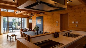 A modern kitchen with wooden cabinetry, a large island with a sink, and a dining area with a table and chairs. - IZA oumimaiko (Otsu)