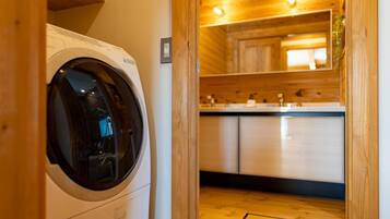 A laundry room with a front-loading washing machine, wooden cabinets, and a sink.
