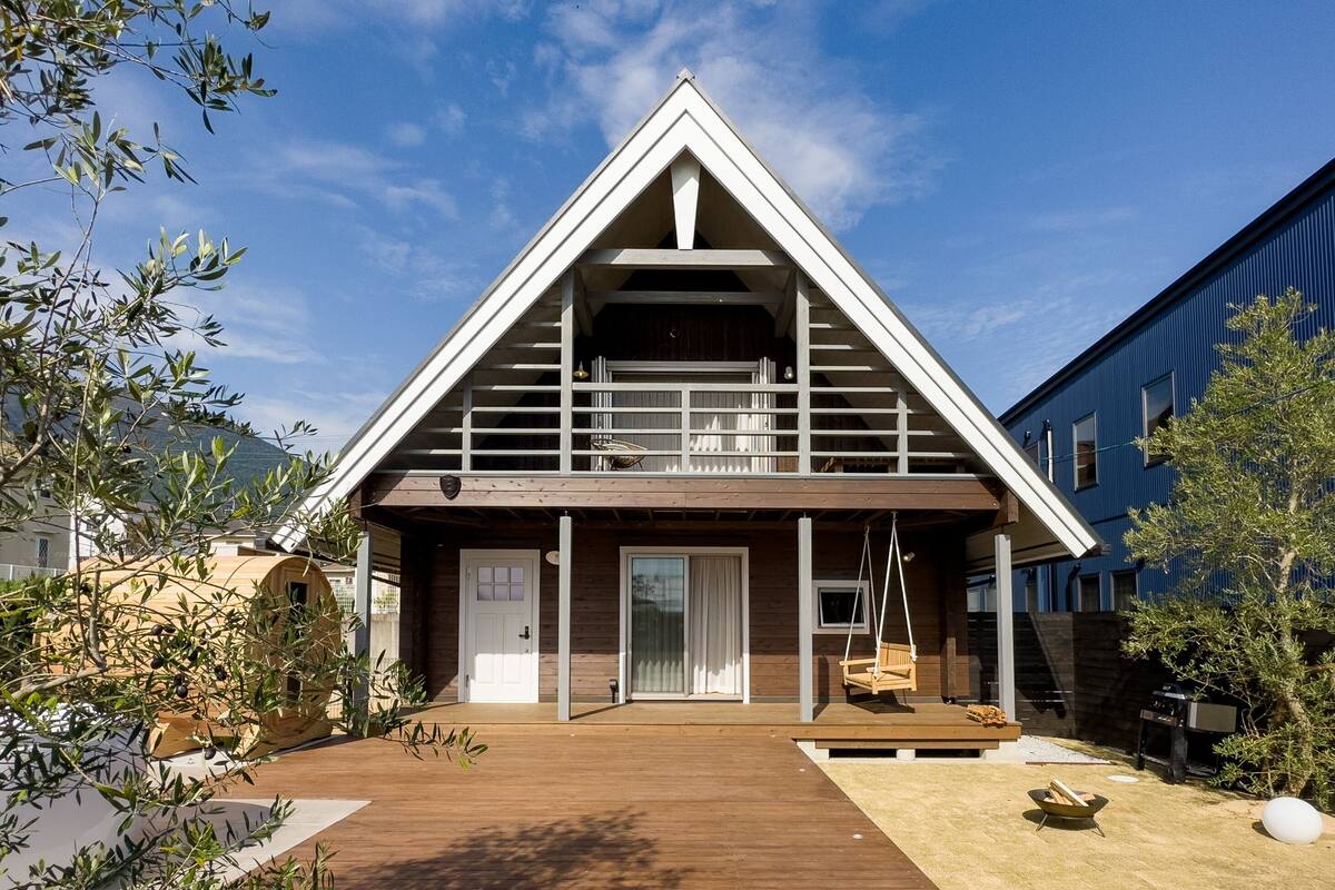Ein modernes Haus mit einem dreieckigen Dach, einer Holterrasse und einer kleinen Veranda mit einer Schaukel.