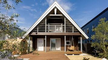 Ein modernes Haus mit einem dreieckigen Dach, einer Holterrasse und einer kleinen Veranda mit einer Schaukel.