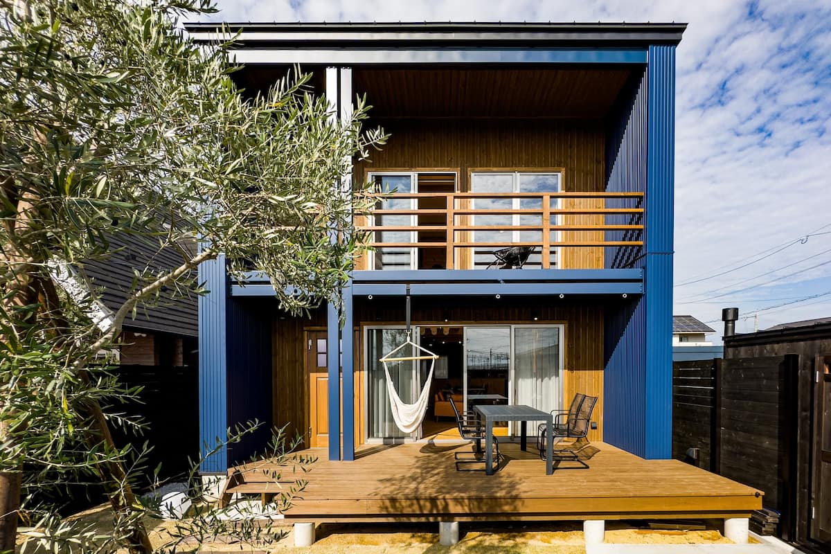 Ein modernes, zweistöckiges Haus mit einer Holzterrasse, einer Hängematte und einem Essbereich.
