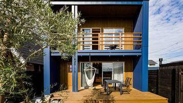A modern two-story house with a wooden deck, a hammock, and a dining area.