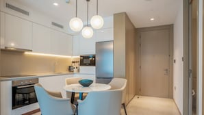 A modern kitchen with white cabinets, a built-in oven, a microwave, and a dining area with a round table and two chairs. - Zapbed House - ADP 2108 (Dubai)