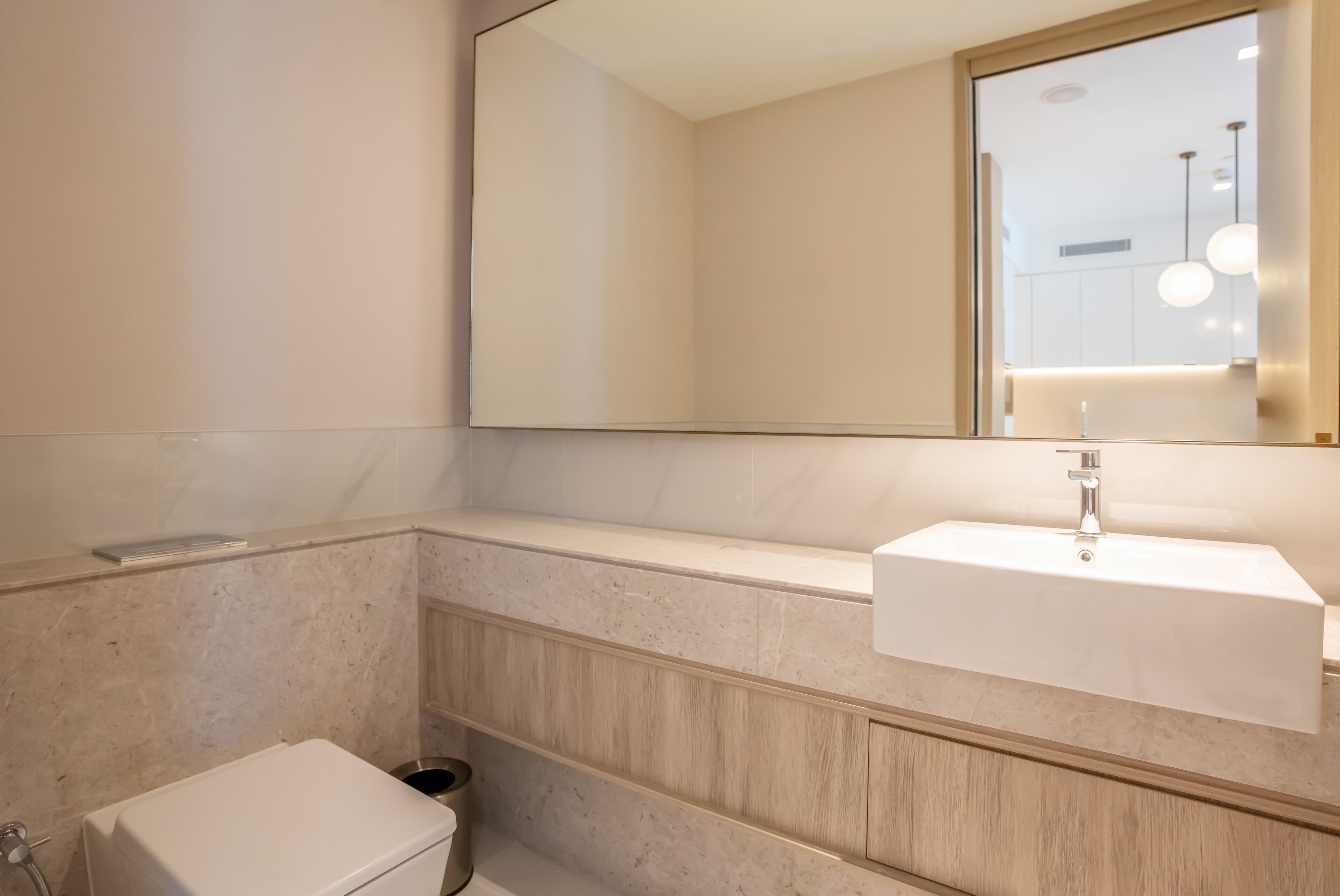 A modern bathroom with a large mirror, a built-in sink, and a toilet.