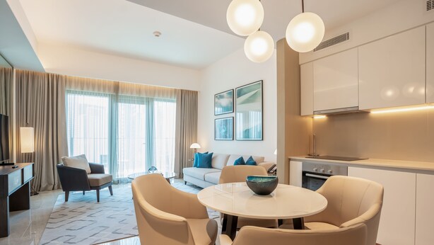 A modern hotel room with a dining area, a sofa set, a TV, and a kitchen area. - Zapbed House - ADP 2108 (Dubai)