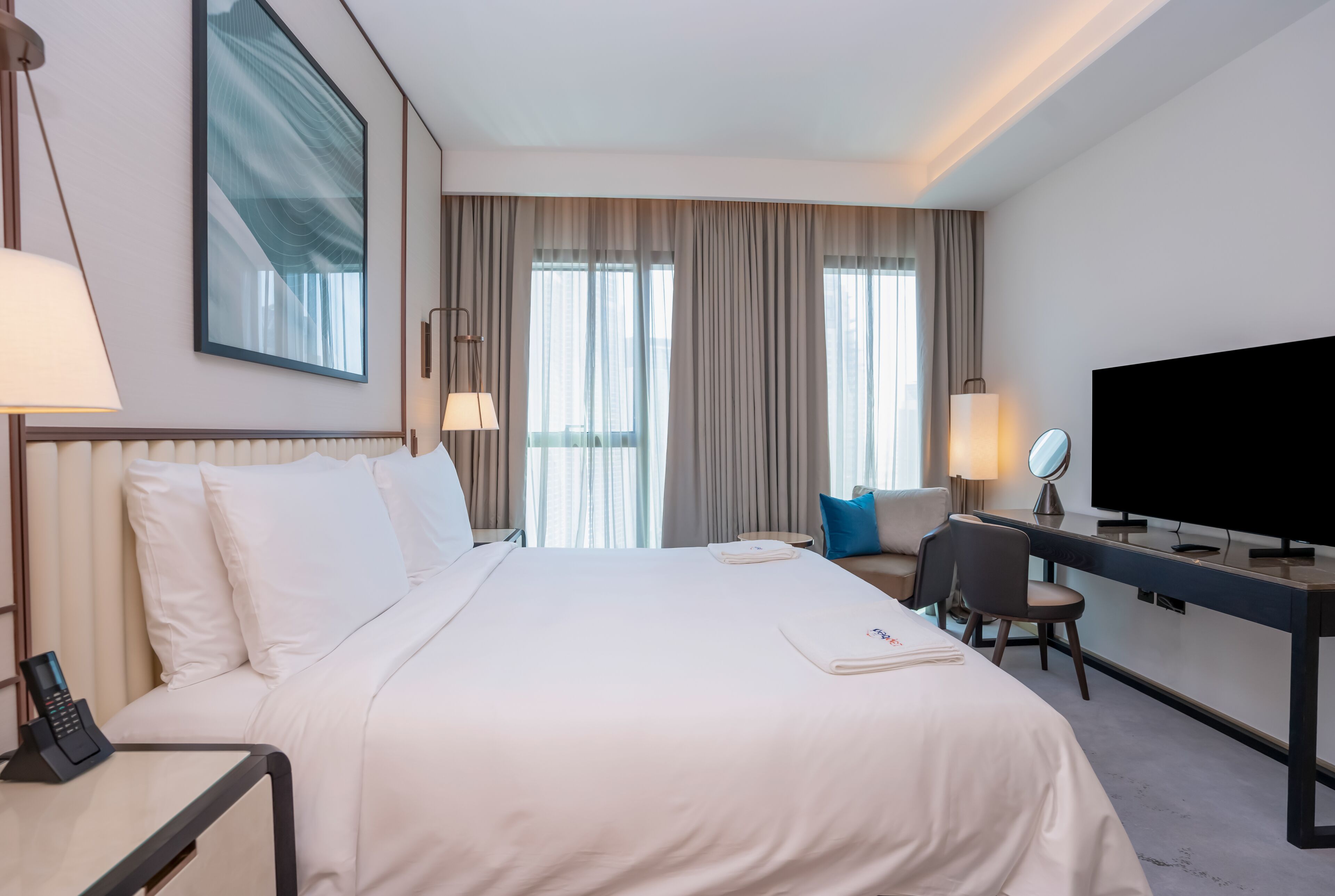 Une chambre d’hôtel comprenant un lit, une table de chevet, une lampe, une télévision, un bureau, une chaise et des rideaux.