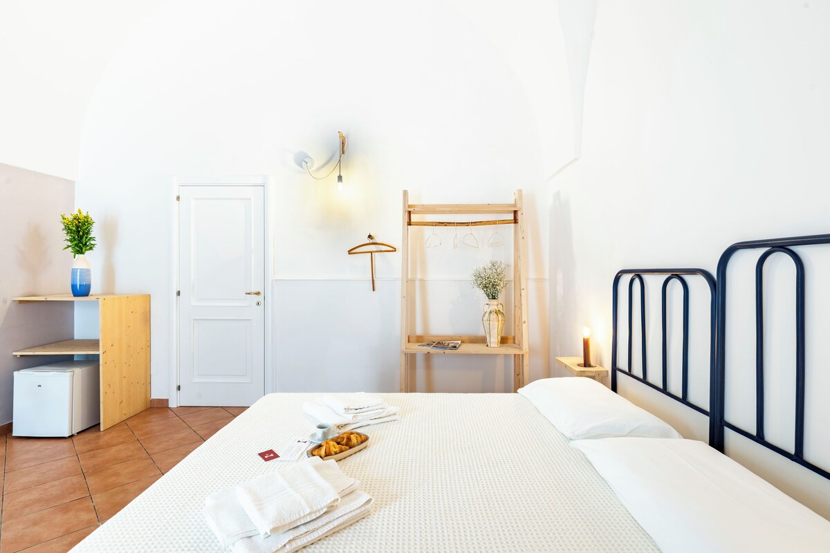 A neatly arranged bedroom with a bed, bedside table, and a small desk with a lamp.