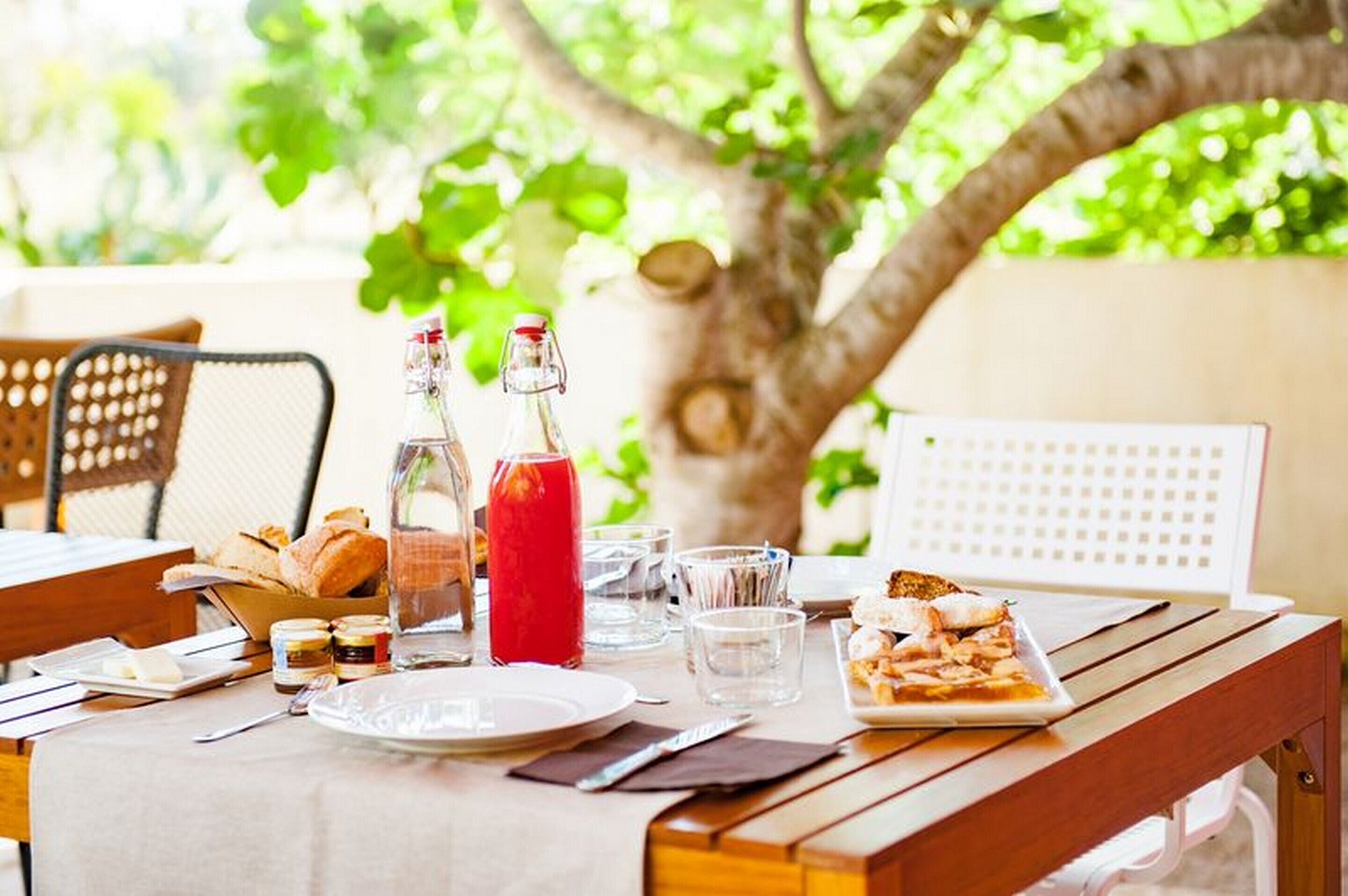 An outdoor dining table with a variety of food items, including bread, a plate of pizza, and condiments.