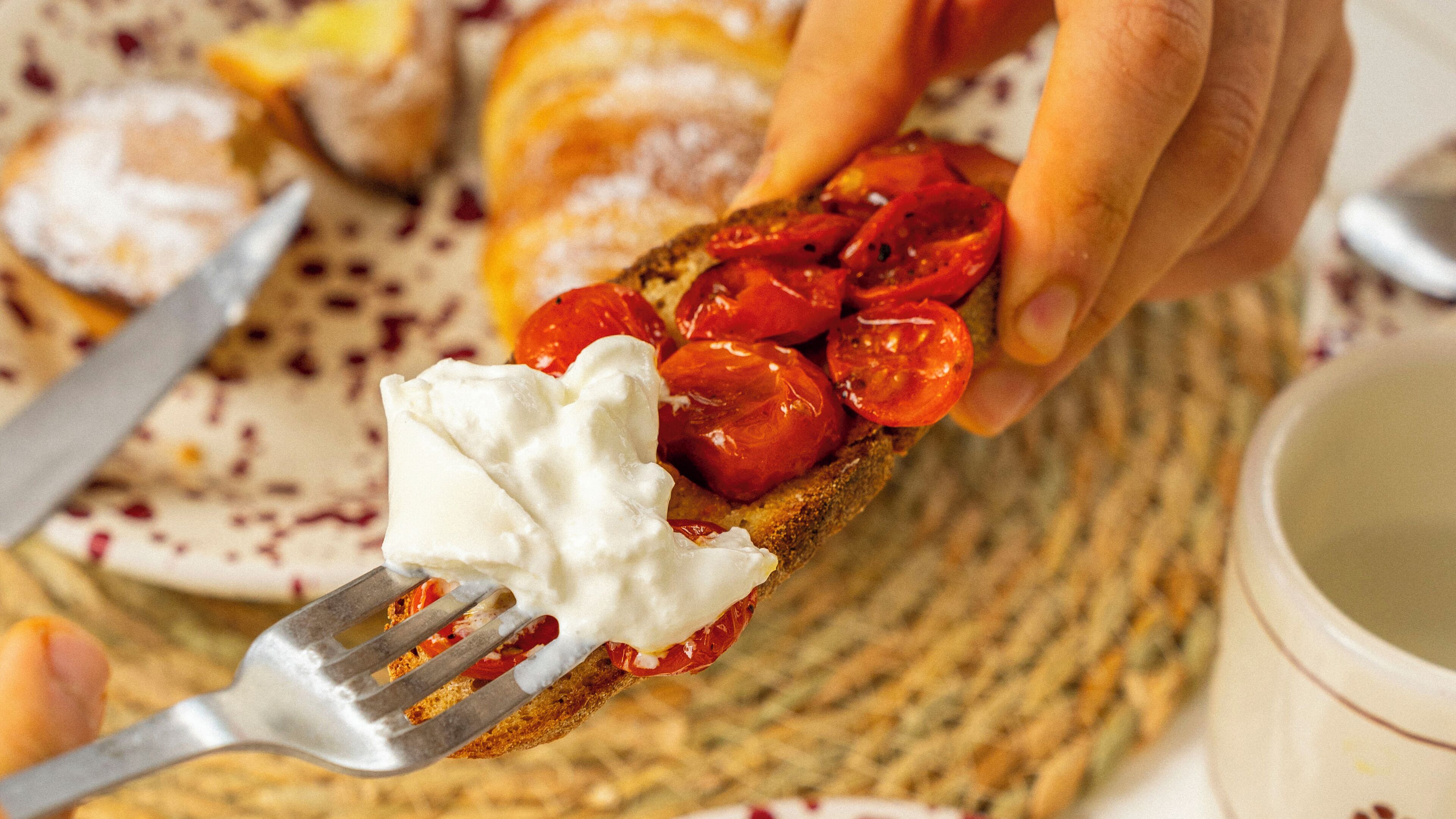Une main tenant une tranche de pain grillé garnie de tomates et d’une cuillère de crème.