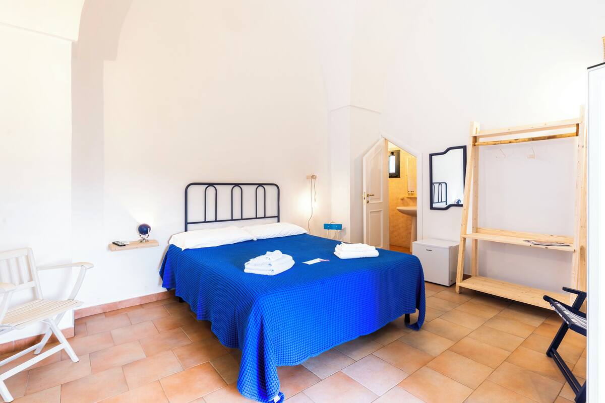 A bedroom with a bed, a chair, a desk, and a wardrobe.