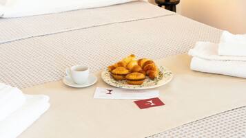 Una cama bien hecha con un plato de cruasanes, una taza de café y una tarjeta de presentación sobre una colcha con textura.