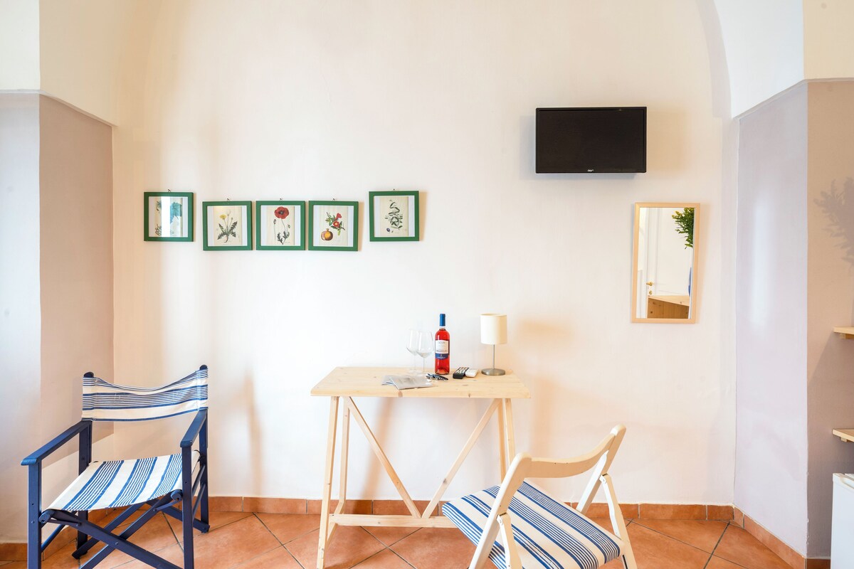 A small room with two chairs, a table with a bottle and glasses, and four framed pictures on the wall.