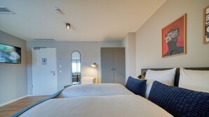 Ein modernes Hotelzimmer mit einem großen Bett, einem Spiegel, einem Kleiderschrank und einem Bild an der Wand.