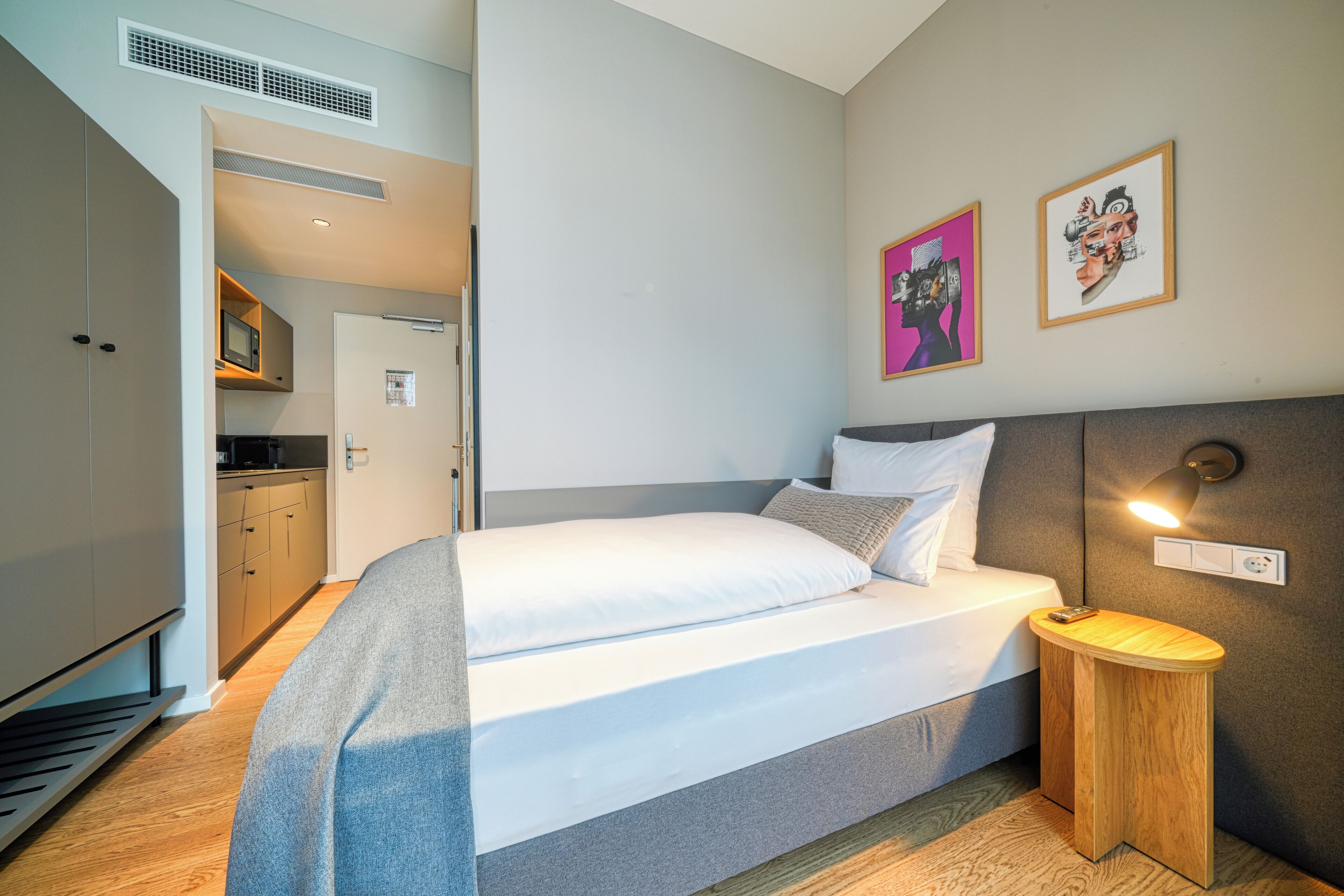 Een moderne slaapkamer met een bed, nachtkastje en uitzicht op de keuken.