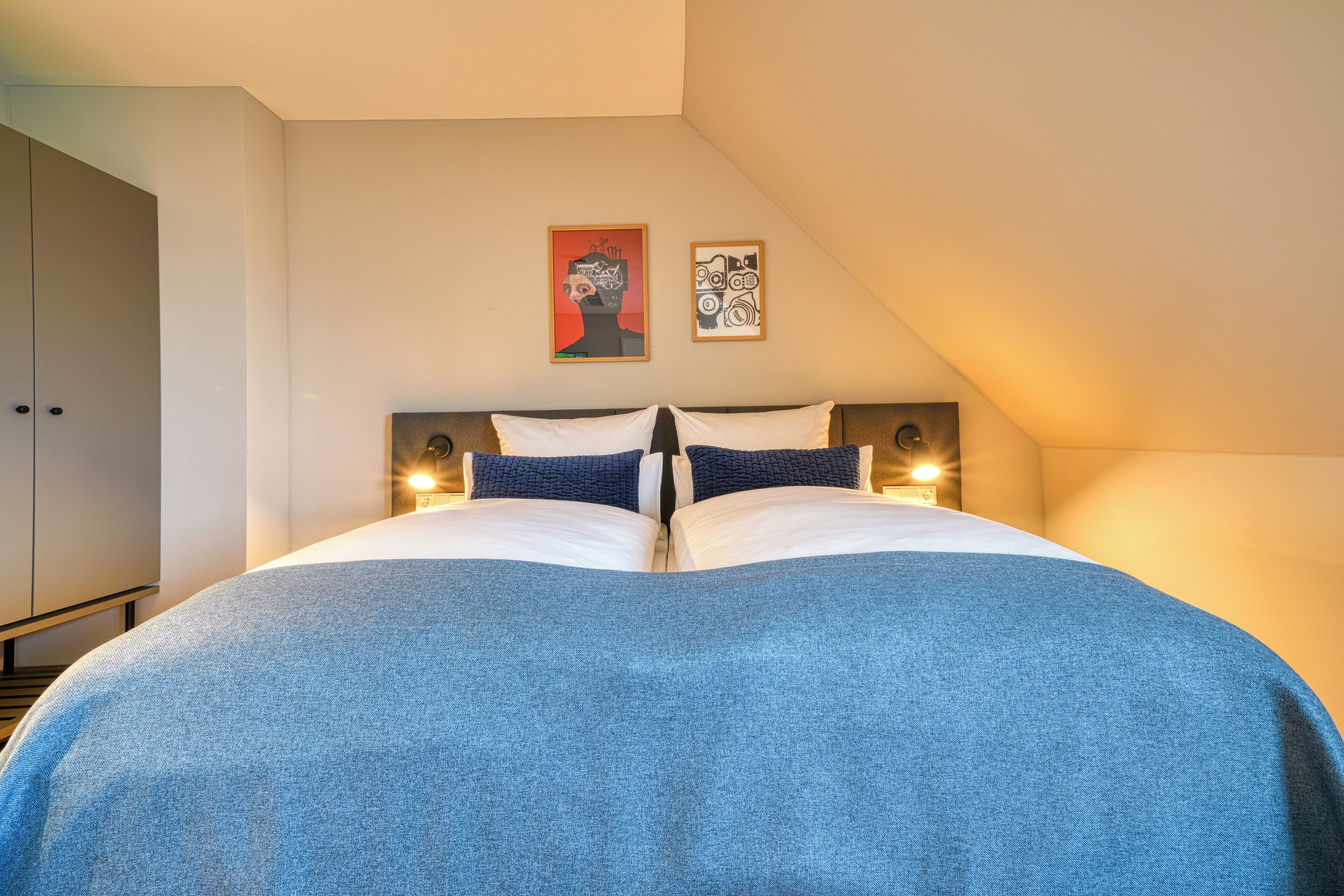 Ein Schlafzimmer mit einem großen Bett, zwei Wandleuchten und zwei gerahmten Kunstwerken an der Wand.
