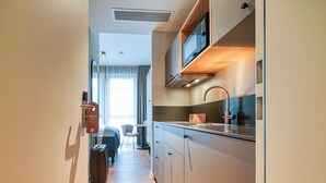 Ein modernes Hotelzimmer mit einer Küchenzeile, einem Bett, einem Koffer und Blick ins Freie.