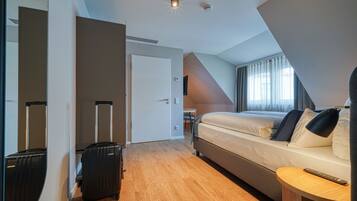 Une chambre d’hôtel moderne équipée d’un lit, d’un bureau, d’une chaise, d’une valise et d’un miroir.