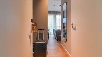 Een hotelgang met houten vloer, een bed op de achtergrond, een tv aan de muur en een koffer.