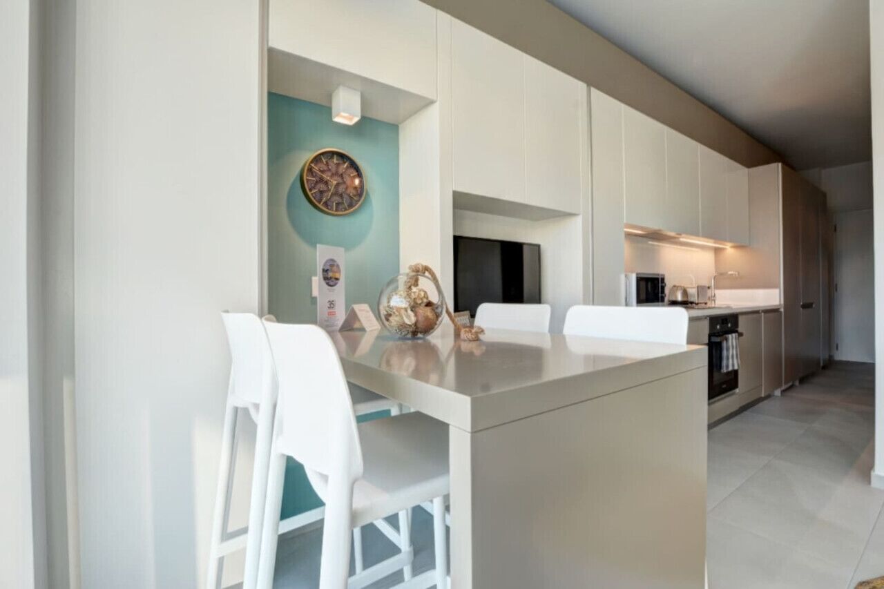 A modern kitchen with white cabinetry, a central island, and a teal accent wall.