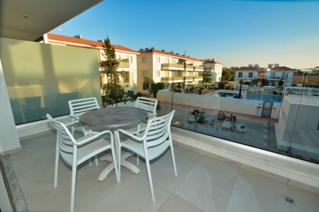 A balcony with a table and chairs, overlooking a pool and residential buildings.