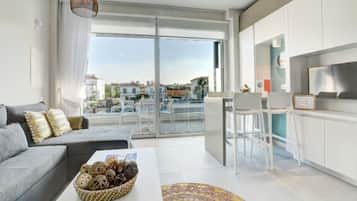 Un salón moderno con un sofá gris, una mesa de centro con una cesta tejida y vistas al exterior a través de puertas de cristal grandes.