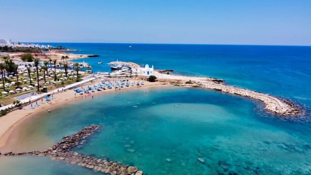 An aerial view of a coastal resort with a clear blue sea, a sandy beach, and a rocky breakwater. - SunnyVillas: 3BR Family Villa☆Private Pool (Protaras)