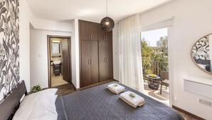 A bedroom with a bed, a wardrobe, a bathroom, and a balcony with a table and chairs. - SunnyVillas: 3BR Family Villa☆Private Pool (Protaras)