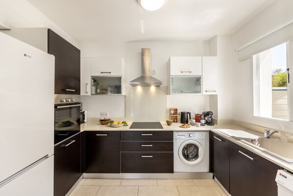 A modern kitchen with a built-in oven, microwave, and washing machine, along with a window providing natural light.