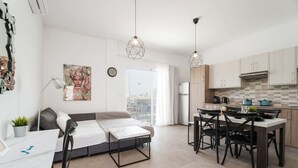 A modern apartment with a dining area, kitchen, and a bed with a desk.