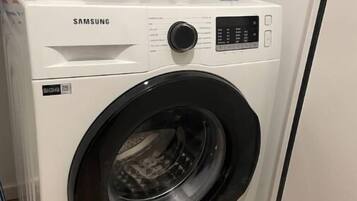 A Samsung front-loading washing machine in a laundry room with a white sink and a faucet above it.