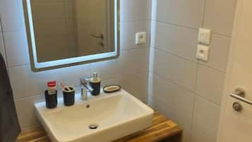 Een badkamer met een wit wastafel, een spiegel met verlichting, en twee zwarte vuilnisbakken.