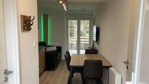 A narrow hallway leading to a dining area with a wooden table and chairs, a kitchen in the background, and a door with a coat rack. - Appartement - Au Cœur du Lac Blanc (Orbey)