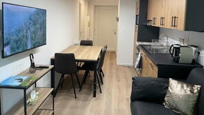 A modern kitchen with wooden cabinets and a black countertop, a dining area with a wooden table and chairs, and a TV mounted on the wall. - Appartement - Au Cœur du Lac Blanc (Orbey)