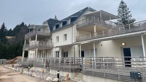 A multi-story residential building with balconies and a construction site in front. - Appartement - Au Cœur du Lac Blanc (Orbey)
