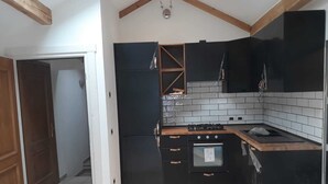 Une cuisine compacte avec des meubles noirs, un pare-feu en carreaux, un four encastré et un plan de travail en bois.