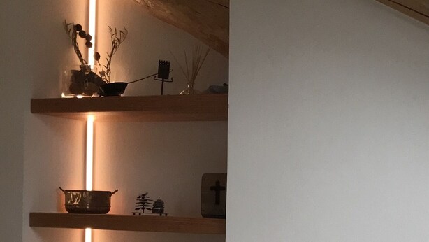 Une pièce avec un plafond en bois, un mur blanc et une étagère contenant divers objets, notamment une boîte de mouchoirs, un bol et des objets décoratifs.