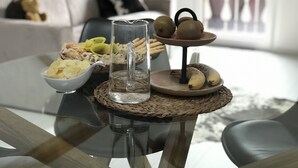 Une table à manger avec un pichet en verre transparent, un bol de chips et un présentoir à fruits contenant des kiwis et des bananes.