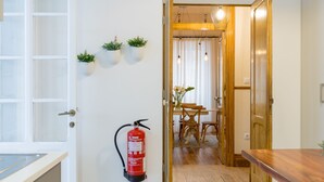 Hotellihuone, jossa on puinen ovi, seinälle asennettu palosammutin ja ruokailutila, joka näkyy oviaukon läpi.