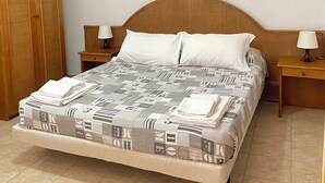 A neatly made bed with a patterned bedspread, two bedside tables with lamps, and a wooden wardrobe. - Riviera Village (Butera)