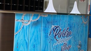 A reception desk with a nautical theme, including a lifebuoy and anchor design, and a sign reading "Riviera Village." - Riviera Village (Butera)