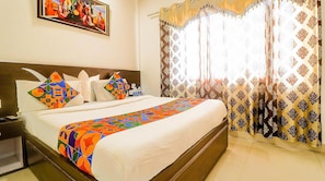 A hotel room with a large bed, a nightstand, a painting on the wall, and patterned curtains. - Hotel Star Metro Inn By GRB (Amritsar)