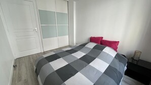 A bedroom with a checkered bedspread, a wardrobe with frosted glass doors, and a bedside table with a lamp. - Appartement Avec Terrasse Proche de Paris et La Défense (Puteaux)