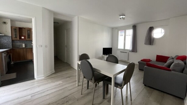 A modern living room with a dining area, a grey sofa, and a kitchen visible through an open doorway. - Appartement Avec Terrasse Proche de Paris et La Défense (Puteaux)