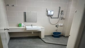 Un baño con un lavamanos blanco, un espejo, un cabezal de ducha manual y un cubo azul.