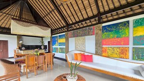 A spacious living area with a high ceiling, a dining area with wooden furniture, and colorful abstract art on the walls. - Belvilla Bunga Matahari Ceking Rice Terrace (Taro)