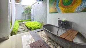 A modern bathroom with a freestanding bathtub, a shower, and a colorful abstract painting on the wall. - Belvilla Bunga Matahari Ceking Rice Terrace (Taro)