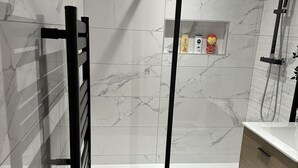 A modern bathroom with a glass shower enclosure, a black towel rack, a wooden floor, and a white sink with a wooden cabinet.