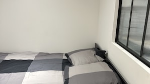 A bed with a checkered bedspread and pillows, a window with blinds, and a plain wall.